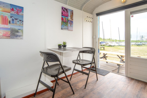 Interno del Tiny wagon presso Marina Parcs Almere, Paesi Bassi, con tavolo, sedie e vista sulle barche.