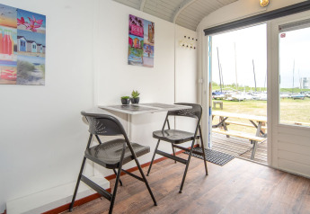 Interior del Tiny wagon en Marina Parcs Almere, Países Bajos, con mesa, sillas y vista a los barcos.