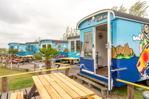 Vagones pequeños y coloridos en Marina Parcs Almere, Países Bajos, con bancos al aire libre y murales de playa.