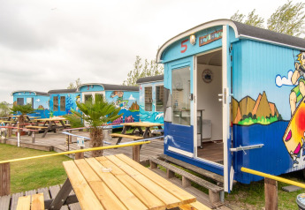 Vagones pequeños y coloridos en Marina Parcs Almere, Países Bajos, con bancos al aire libre y murales de playa.