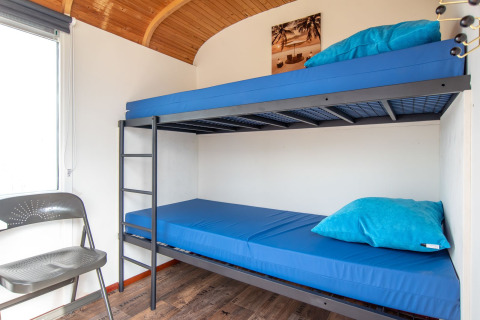 Interior luminoso de Tiny Wagon en Marina Parcs Almere, Países Bajos, con litera y ropa de cama azul.