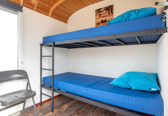 Interior luminoso de Tiny Wagon en Marina Parcs Almere, Países Bajos, con litera y ropa de cama azul.