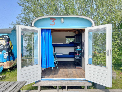 Casa tiny wagon en Marina Parcs Almere, Países Bajos, con puertas abiertas, literas y decoración colorida.