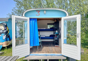 Casa tiny wagon en Marina Parcs Almere, Países Bajos, con puertas abiertas, literas y decoración colorida.