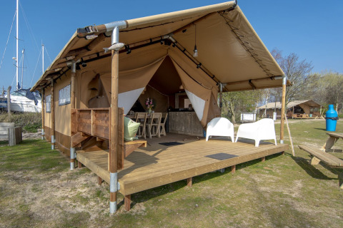 Tenda safari lodge al Marina Parcs Almere, Paesi Bassi, con veranda in legno e sedie bianche all’aperto.