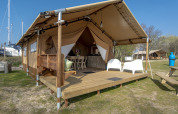Safaritent lodge bij Marina Parcs Almere, Nederland, met houten veranda, stoelen en natuurlijke omgeving.