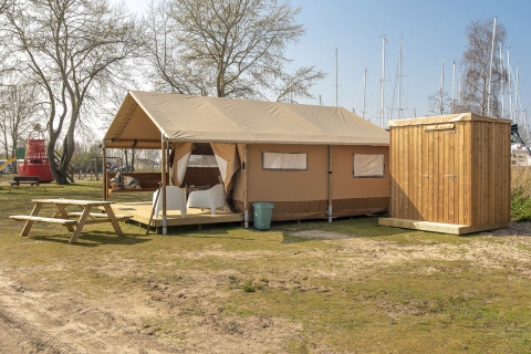 Safari lodge tent met houten schuurtje en picknicktafel bij Marina Parcs Almere, Nederland, nabij boten.