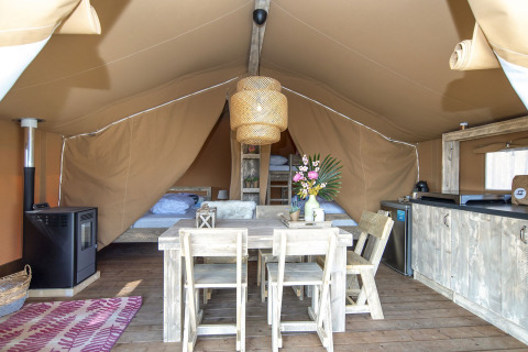 Intérieur d'une tente safari lodge avec meubles en bois rustique, lits, petite cuisine et bouquet de fleurs.