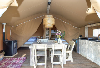 Intérieur d'une tente safari lodge avec meubles en bois rustique, lits, petite cuisine et bouquet de fleurs.