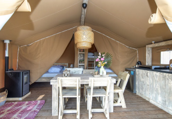 Intérieur d'une tente safari lodge avec meubles en bois rustique, lits, petite cuisine et bouquet de fleurs.