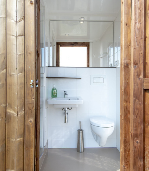 Moderne badkamer met houten deur, hangtoilet en wastafel in een safari lodge bij Marina Parcs Almere.