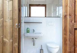 Moderne badkamer met houten deur, hangtoilet en wastafel in een safari lodge bij Marina Parcs Almere.
