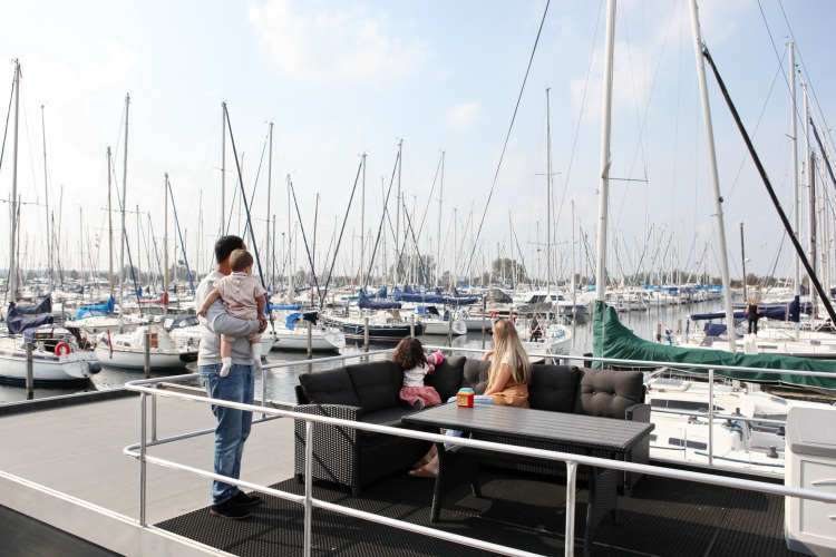 Familia disfruta en la houseboat 4-Almere en Marina Parcs Almere, Países Bajos, rodeados de veleros en el puerto.