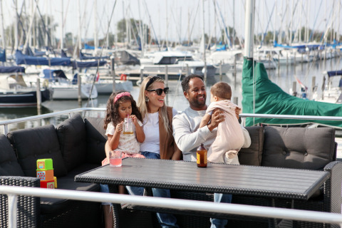 Gezin zit op House boat 4-Almere bij Marina Parcs Almere in Nederland, met jachten op de achtergrond.