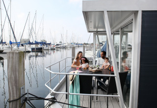 Familia sentada en la terraza de una casa flotante en Marina Parcs Almere, rodeada de veleros en Holanda.