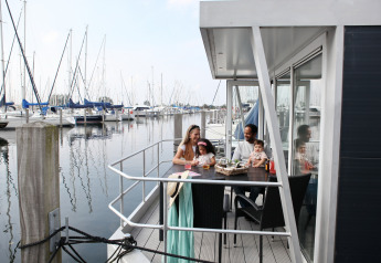 Famiglia seduta sulla terrazza di una casa galleggiante a Marina Parcs Almere, con barche a vela vicine.