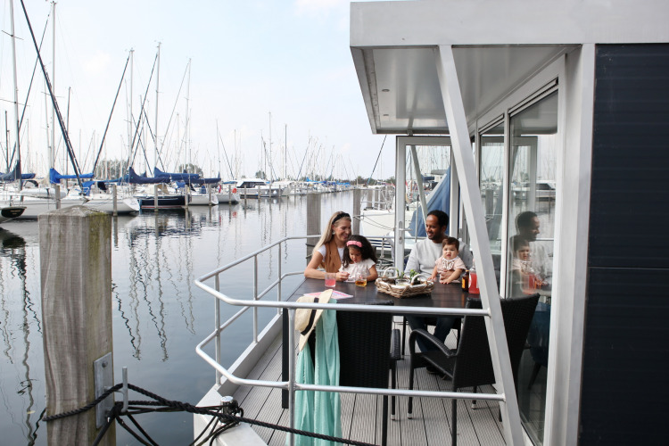 Familia sentada en la terraza de una casa flotante en Marina Parcs Almere, rodeada de veleros en Holanda.