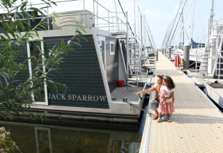 De woonboot Jack Sparrow bij Marina Parcs Almere in Nederland, met twee meisjes op de steiger dichtbij.