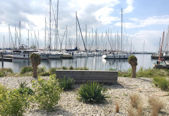 Zicht vanaf House boat 4-Almere aan Marina Parcs Almere met bankje, planten en zeilboten in Nederland.