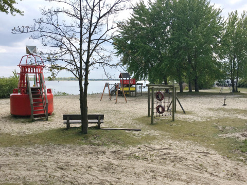 Speelplein aan zandstrand, rode boei en bomen bij het meer bij House boat 4-Almere in Nederland.