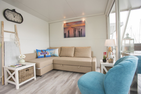 Lichte, moderne woonkamer van een woonboot bij Marina Parcs Almere met beige bank en blauwe stoel.