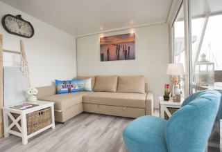 Lyst og moderne stue på husbåd i Almere Marina Parcs, med beige sofa, blå stol og havudsigt.