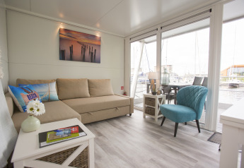 Interno della House boat 4-Almere al Marina Parcs Almere nei Paesi Bassi, con divano e ampie finestre.