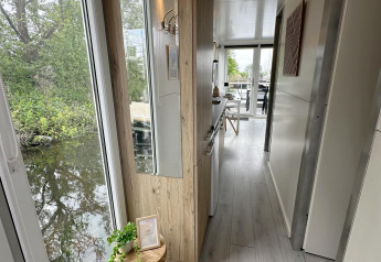 Corridoio interno di una casa galleggiante con grandi finestre, vista sull’acqua e legno chiaro ad Almere.