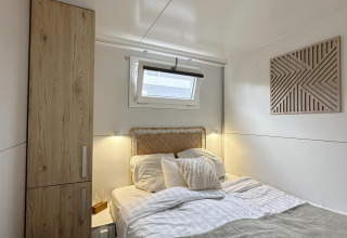 Acogedor dormitorio en una casa flotante en Almere, Países Bajos, con armario de madera y ventana.