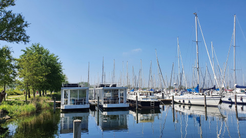 Casa flotante en Marina Parcs Almere, Países Bajos, rodeada de veleros bajo un cielo soleado y azul.