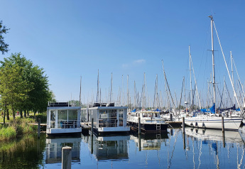Casa flotante en Marina Parcs Almere, Países Bajos, rodeada de veleros bajo un cielo soleado y azul.