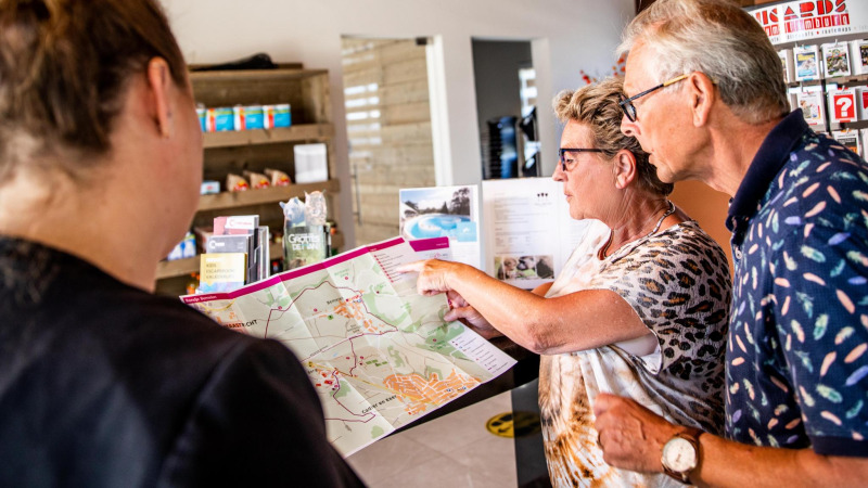 Dos visitantes mayores reciben orientación sobre un mapa en la recepción de Resort Mooi Bemelen, Biebosch-tuinhuis.