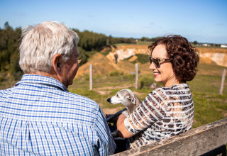 Una pareja mayor con su perro sentados en un banco en Biebosch - tuinhuis, Resort Mooi Bemelen, Países Bajos.
