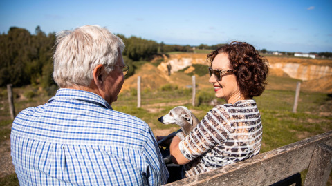Una pareja mayor con su perro sentados en un banco en Biebosch - tuinhuis, Resort Mooi Bemelen, Países Bajos.