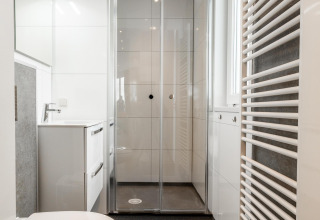 Baño moderno con ducha, inodoro blanco y lavabo en Biebosch - tuinhuis en Resort Mooi Bemelen, Países Bajos.