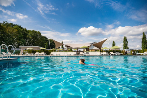 Persona nadando en la piscina exterior de Biebosch - tuinhuis en Resort Mooi Bemelen, Países Bajos, bajo el sol.