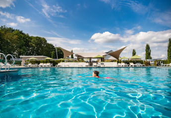 Person svømmer i udendørs pool ved Biebosch - tuinhuis på Resort Mooi Bemelen, Holland, under blå himmel.
