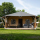 Safari tent with covered porch, barbecue, patio seating, and hammock on a grassy lawn in a natural setting.