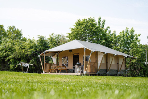 Tienda safari Villatent Cottage en Camping Borken am See, Alemania, rodeada de césped y árboles verdes.