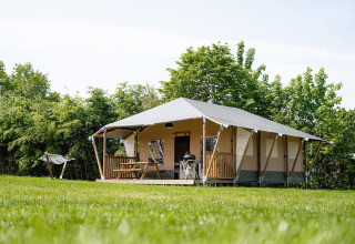 Tienda safari Villatent Cottage en Camping Borken am See, Alemania, rodeada de césped y árboles verdes.