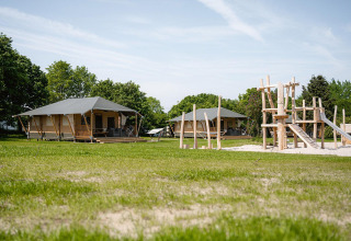 Tente safari Villatent Cottage au Camping Borken am See en Allemagne avec aire de jeux et verdure.
