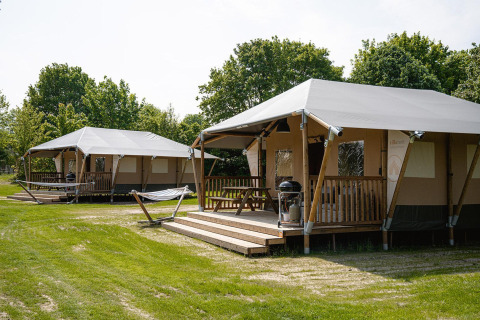 Deux tentes safari Villatent Cottage avec terrasse et barbecue au Camping Borken am See, entourées d’arbres.
