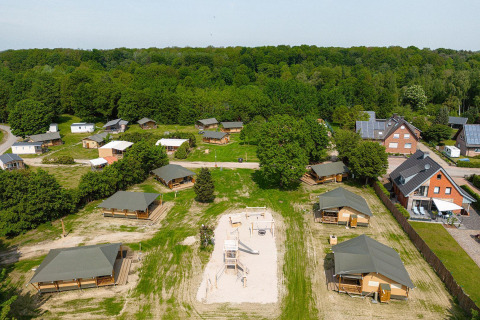 Vista aérea de tiendas safari Villatent Cottage y área de juegos en Camping Borken am See, Alemania, rodeado de naturaleza.