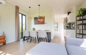 Lyst og moderne lodge-interiør med spisebord, seks stole, køkken og store vinduer med masser af dagslys.