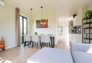 Modern lodge-interieur met veel licht, een eettafel, zes stoelen, keuken en grote ramen voor zoninval.