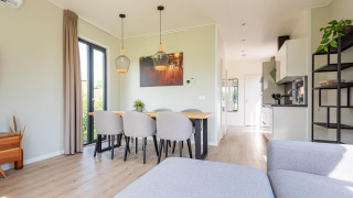 Modernes Lodge-Interieur mit Esstisch, sechs Stühlen, heller Küche und großen Fenstern voller Tageslicht.