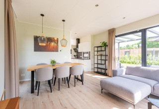 Moderne lodge met open leefruimte, eettafel, zetel en grote ramen met zicht op de tuin overdag.