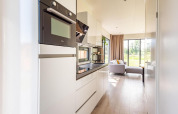 Modernes Lodge-Küchenbereich mit weißen Schränken, Einbaugeräten und Blick auf Wohnzimmer und Garten.