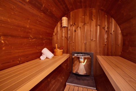 Vue intérieure d’un sauna en bois dans un lodge avec des bancs, des serviettes, un seau et un poêle.