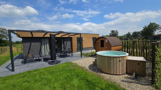 Foto exterior de un lodge moderno con terraza, sauna de madera y jacuzzi en un césped verde.